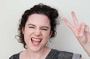 Best Australian female voiceover artist you can hire smiling really big and throwing the peace sign with her hand. She seems like a lot of fun to work with!